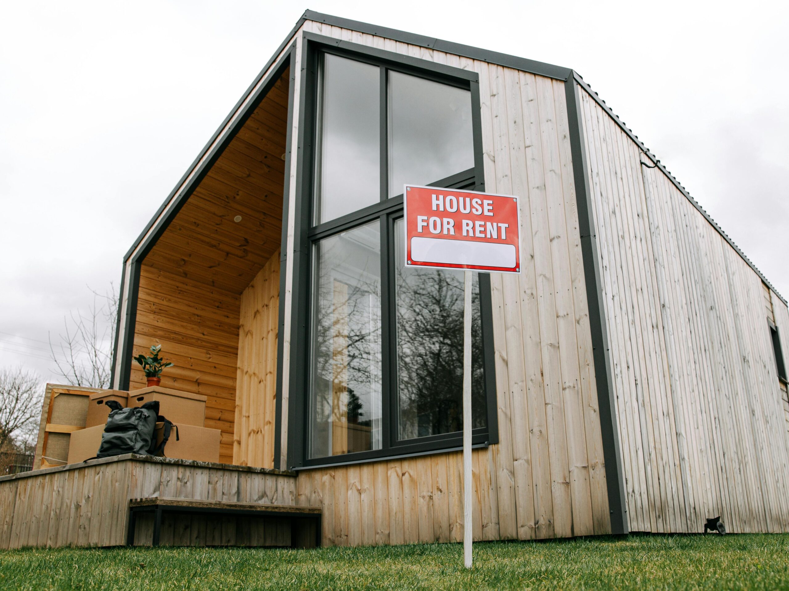 Low-angle view of a modern wooden house with a 'House for Rent' sign, showcasing contemporary architecture.